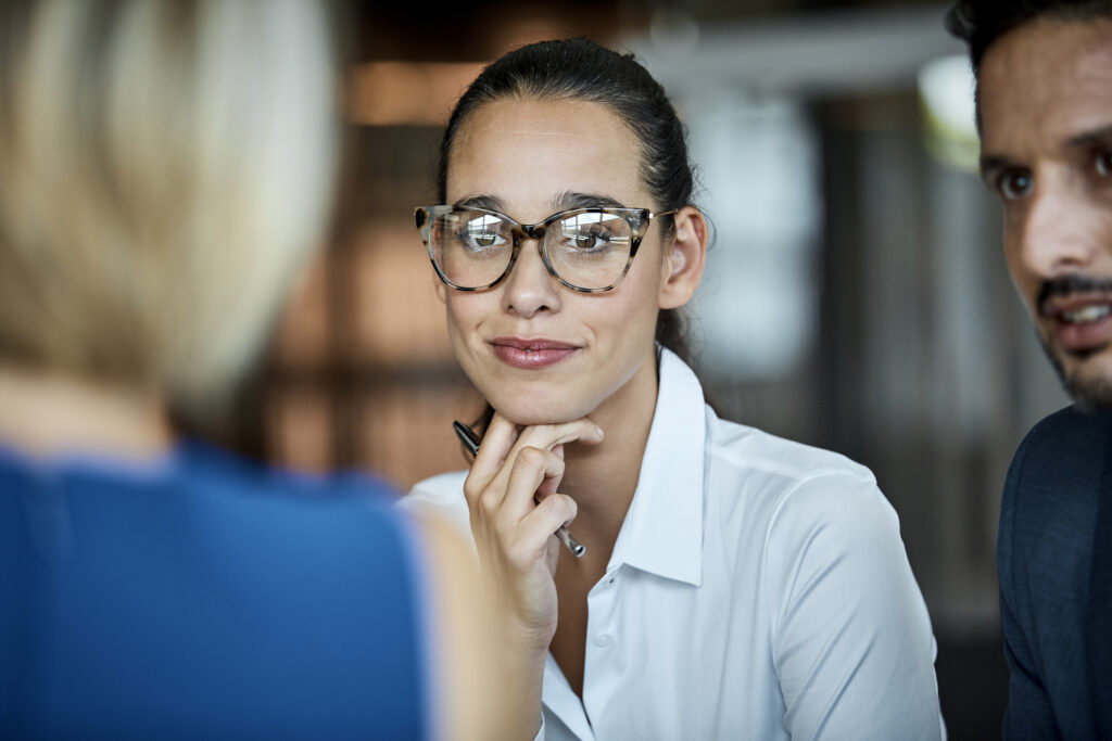 Confident businesswoman looking at female colleague. Professionals are sitting in textile factory. Male and female executives are working together.